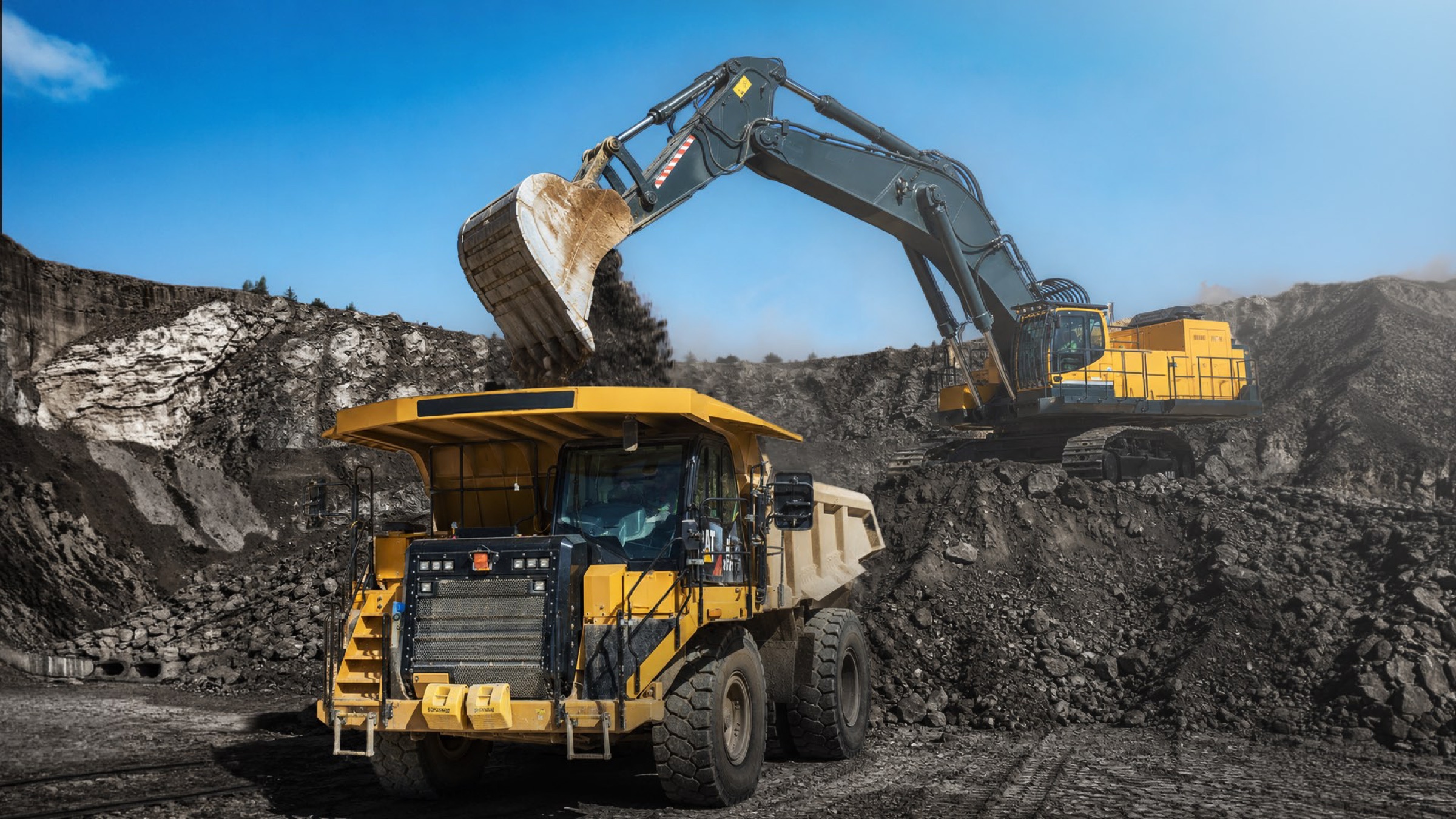 Excavator loading overburden into a haul truck at the pit face